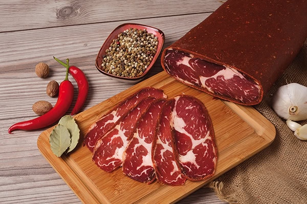 Pastırma dilimleri, tahta üzerinde baharatlarla. Yanında biber, defne yaprağı ve sarımsak ile doğal sunum.