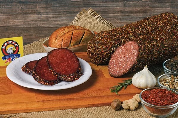 Ahşap zemin üzerine sucuk dilimleri, ekmek, sarımsak, baharat ve bütün sucuk yerleştirilmiş.